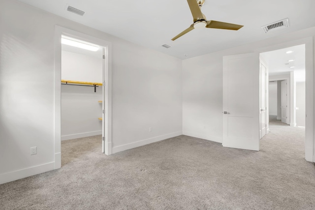 unfurnished bedroom featuring a walk in closet, ceiling fan, a closet, and light carpet