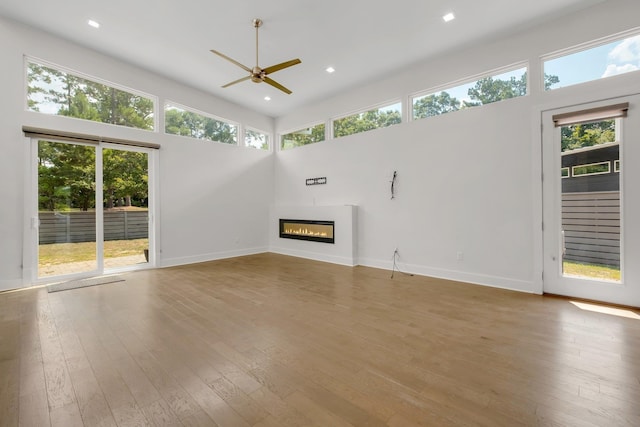 unfurnished living room featuring hardwood / wood-style floors, ceiling fan, a healthy amount of sunlight, and a high ceiling