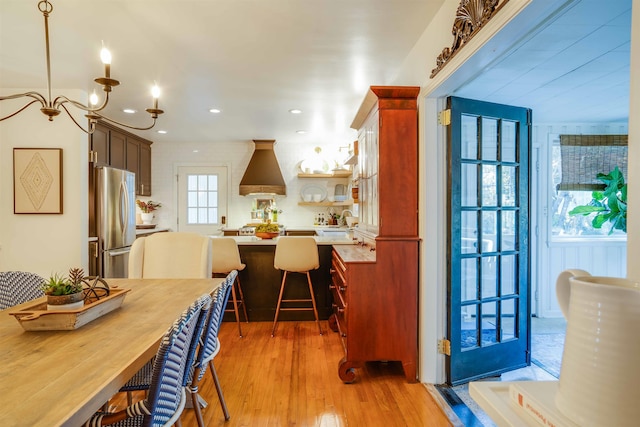 kitchen featuring hanging light fixtures, stainless steel fridge, a notable chandelier, and light hardwood / wood-style floors