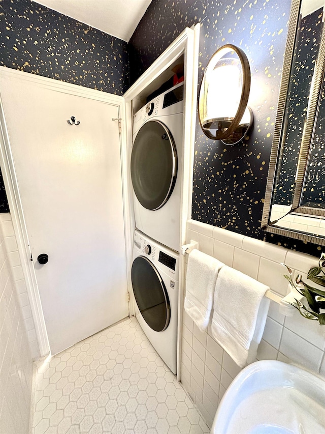 clothes washing area with light tile patterned floors, stacked washer and dryer, and tile walls