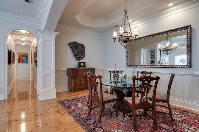 dining room with an inviting chandelier, light hardwood / wood-style flooring, decorative columns, a tray ceiling, and crown molding