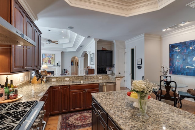 kitchen with appliances with stainless steel finishes, sink, light stone counters, and wall chimney range hood