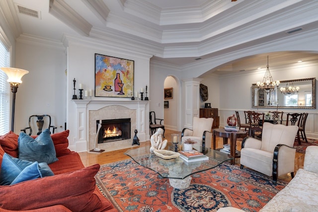 living room featuring hardwood / wood-style flooring, a high end fireplace, crown molding, a tray ceiling, and ornate columns