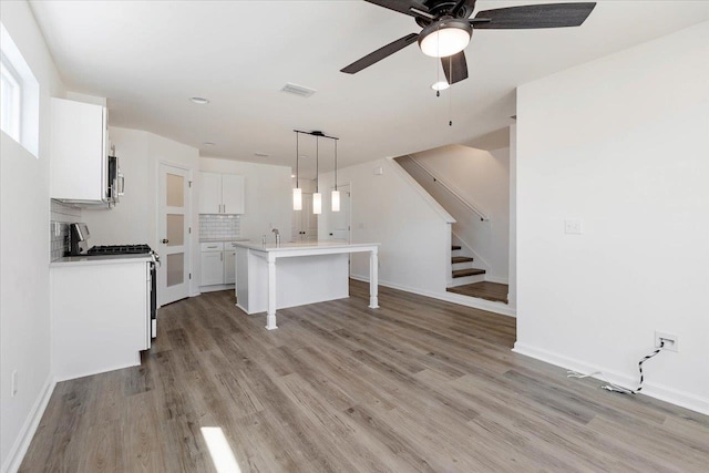 kitchen featuring light wood-type flooring, white cabinetry, hanging light fixtures, white gas stove, and a center island