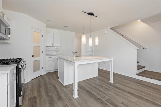 kitchen with stainless steel appliances, pendant lighting, an island with sink, hardwood / wood-style flooring, and white cabinets