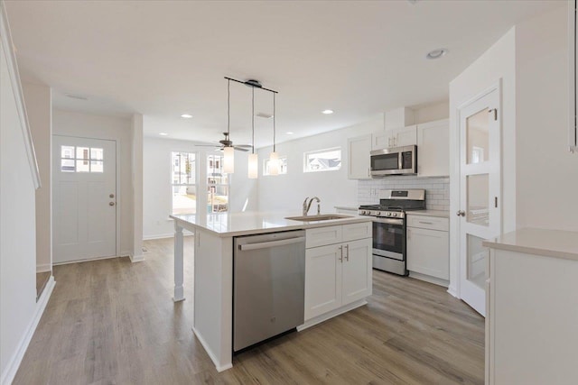 kitchen featuring appliances with stainless steel finishes, pendant lighting, sink, white cabinets, and a kitchen island with sink