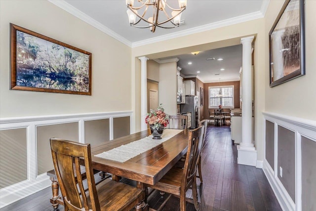 dining room featuring dark wood-type flooring, crown molding, ornate columns, and an inviting chandelier