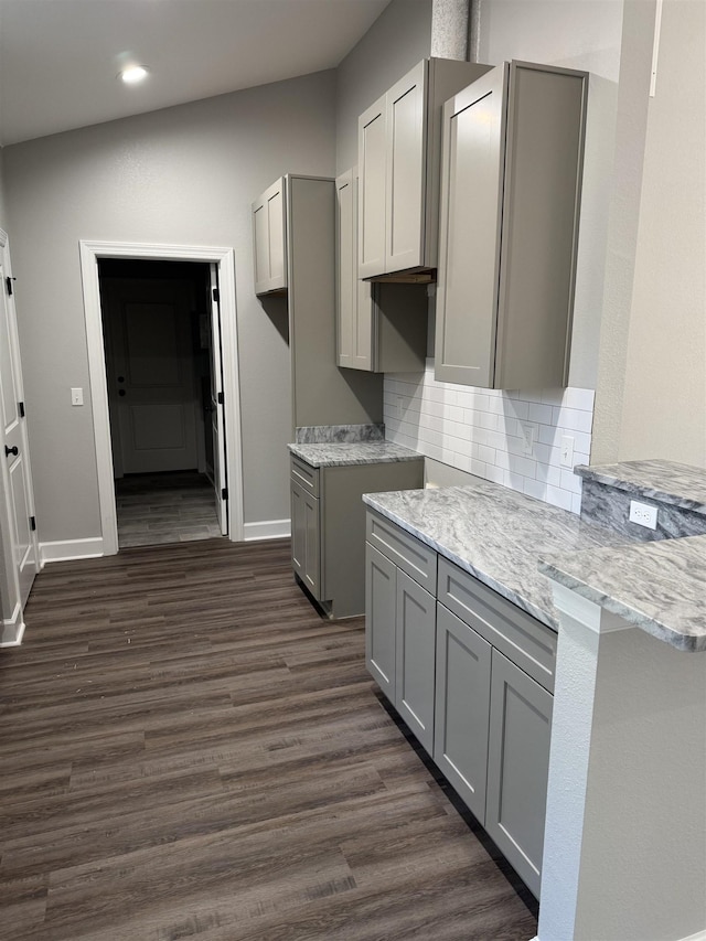 kitchen with kitchen peninsula, decorative backsplash, gray cabinetry, dark wood-type flooring, and light stone countertops