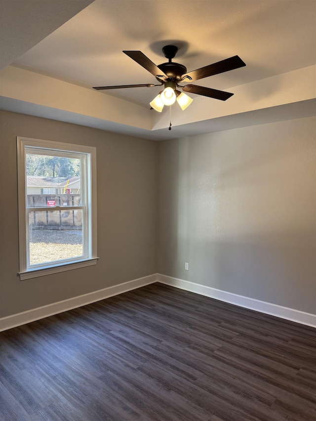 empty room featuring a raised ceiling, ceiling fan, and dark wood-type flooring