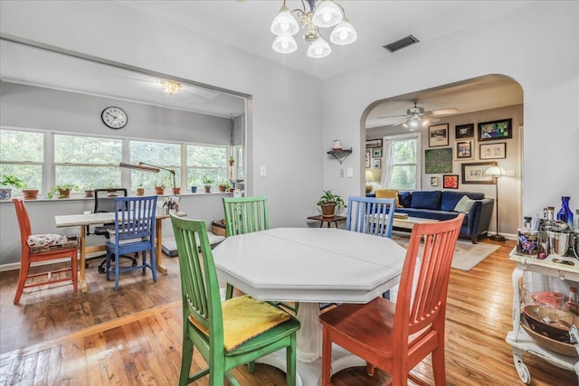 dining area with arched walkways, ceiling fan with notable chandelier, wood finished floors, and visible vents