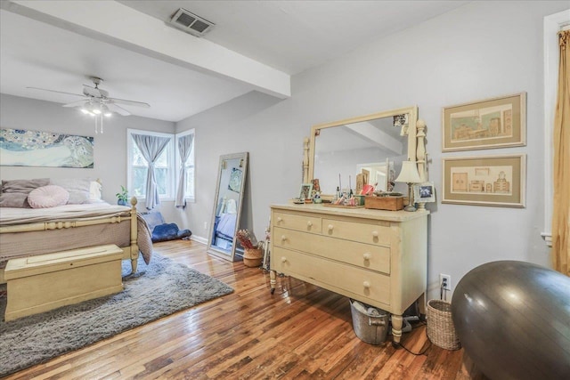 bedroom with ceiling fan, beam ceiling, baseboards, wood finished floors, and visible vents