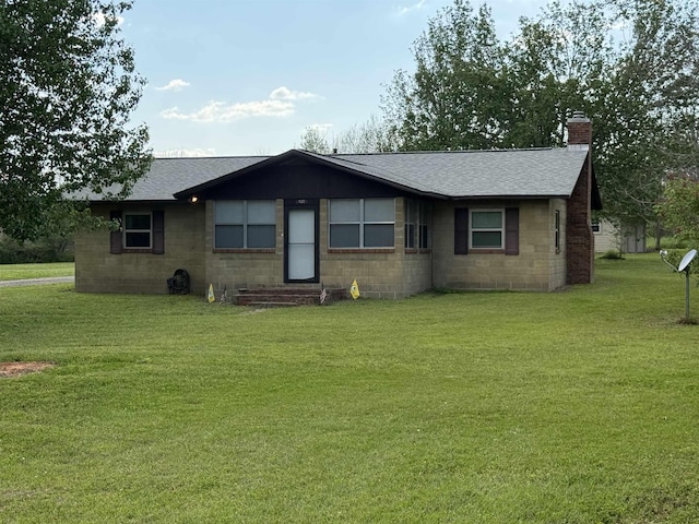 view of front of house with a front yard, concrete block siding, a chimney, and a shingled roof