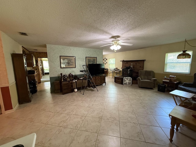 living area with a textured ceiling, ceiling fan, a fireplace, and visible vents