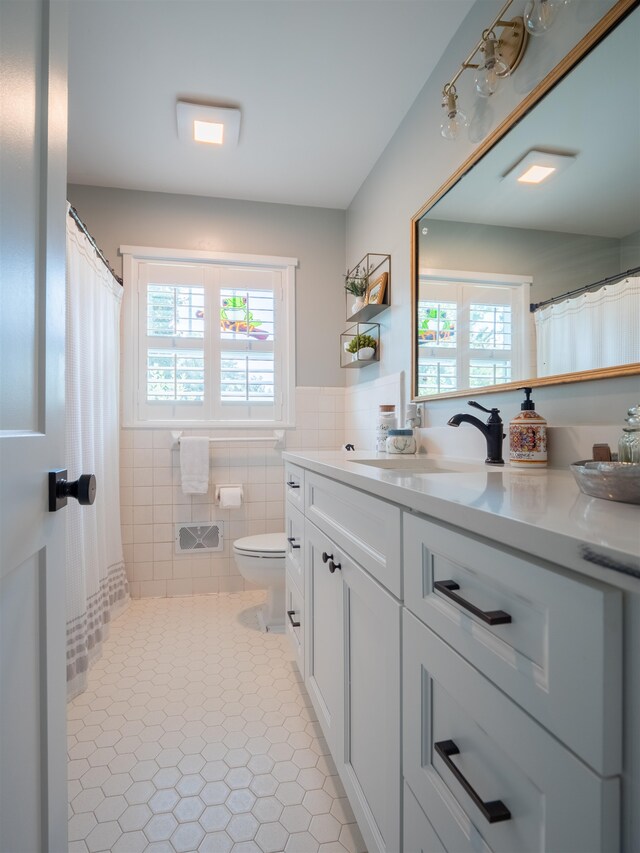 bathroom with tile walls, vanity, tile patterned floors, and toilet