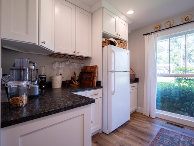 kitchen with dark stone counters, white refrigerator, white cabinets, backsplash, and light wood-type flooring