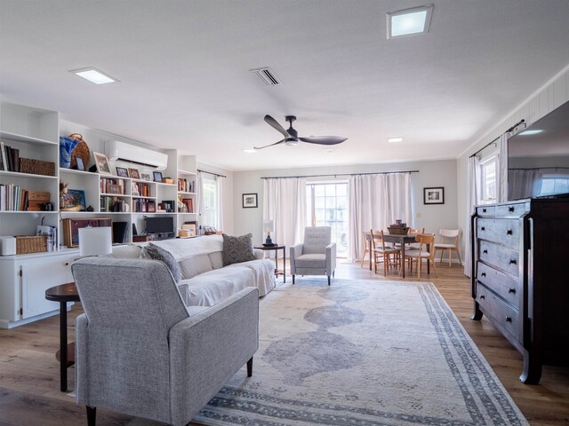 living room with ceiling fan, light hardwood / wood-style floors, and a wall mounted AC