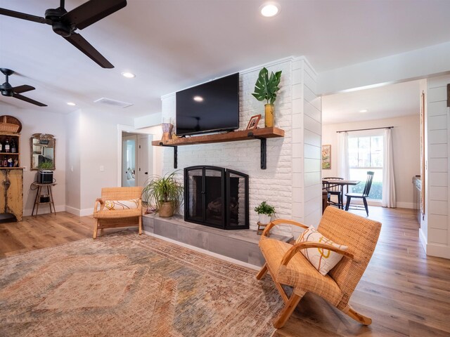 living room with a fireplace, wood-type flooring, and ceiling fan