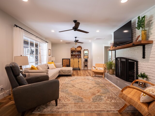 living room with a fireplace, ceiling fan, and light wood-type flooring