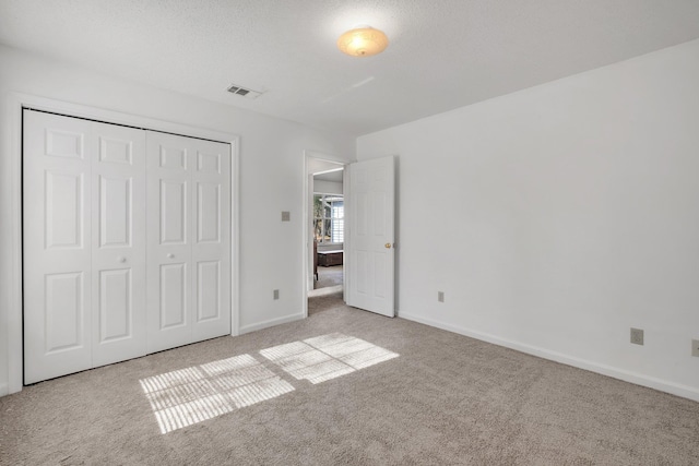 unfurnished bedroom featuring light carpet, a closet, and a textured ceiling