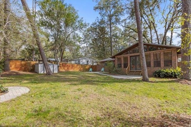 view of yard featuring entry steps, a fenced backyard, an outdoor structure, and a storage shed