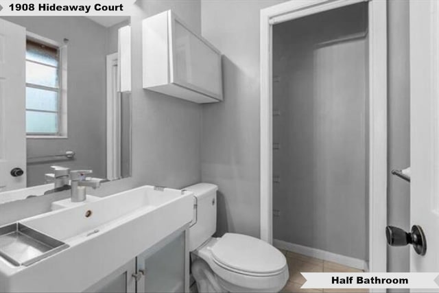 half bathroom with tile patterned flooring, vanity, toilet, and baseboards