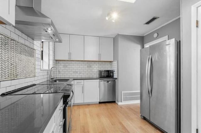 kitchen with stainless steel appliances, dark countertops, white cabinetry, a sink, and wall chimney range hood