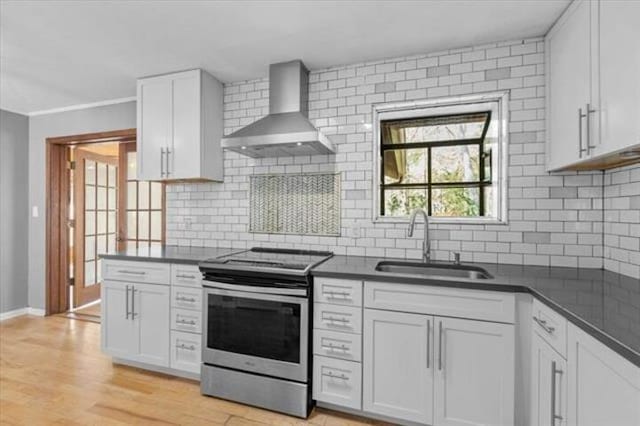 kitchen with dark countertops, white cabinets, a sink, wall chimney range hood, and stainless steel range with electric stovetop