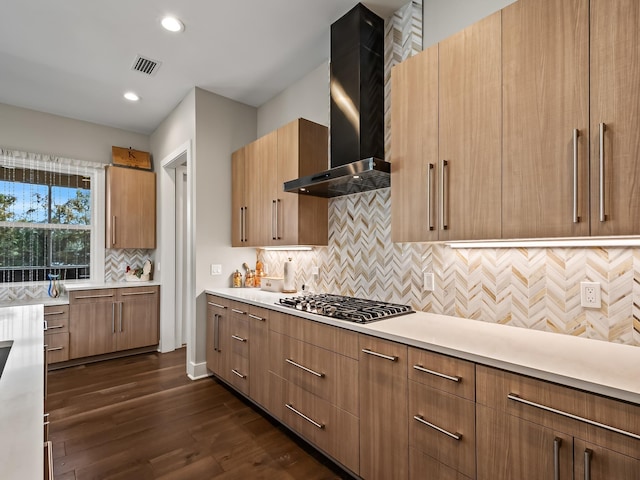 kitchen featuring backsplash, dark wood-type flooring, wall chimney range hood, and stainless steel gas cooktop