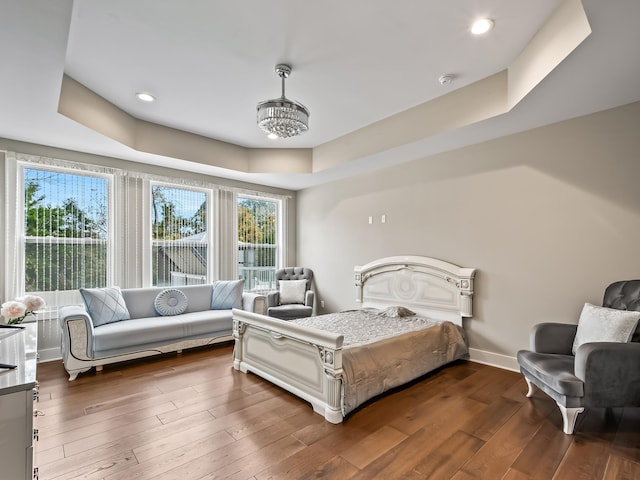 bedroom with a tray ceiling, dark hardwood / wood-style flooring, and an inviting chandelier