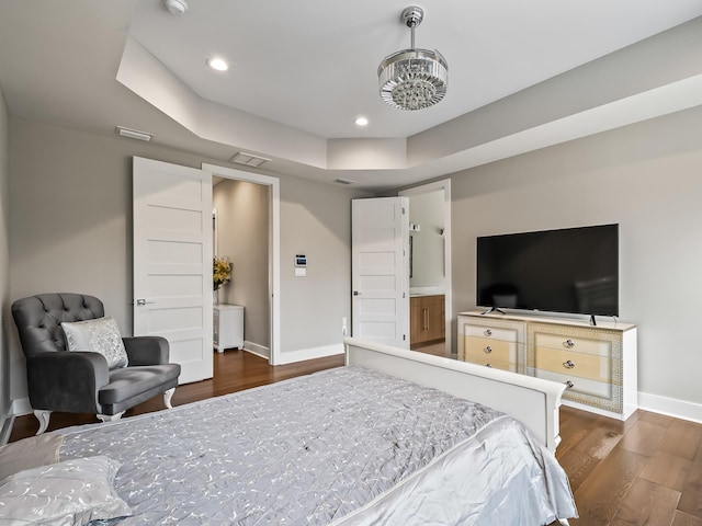 bedroom with a tray ceiling, connected bathroom, and dark wood-type flooring