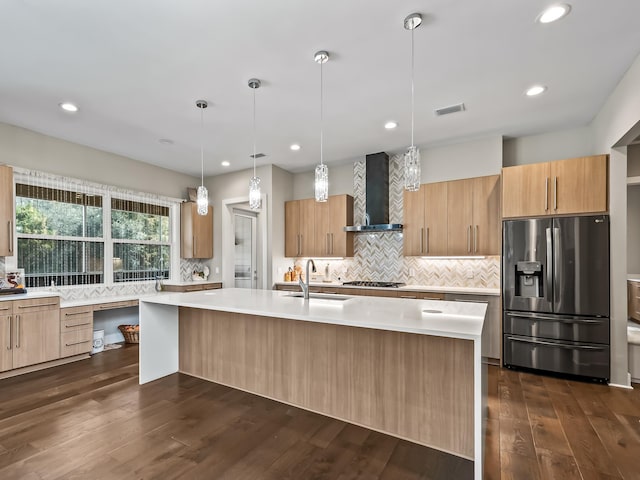 kitchen featuring appliances with stainless steel finishes, a center island with sink, dark hardwood / wood-style floors, and wall chimney range hood