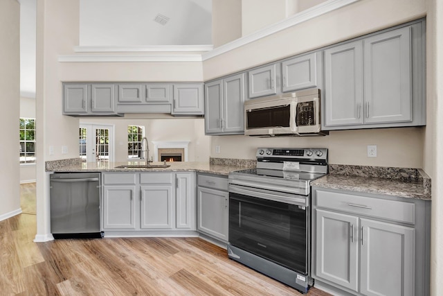 kitchen with gray cabinets, a towering ceiling, sink, stainless steel appliances, and light wood-type flooring