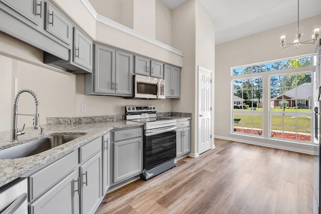 kitchen featuring sink, gray cabinets, stainless steel appliances, light stone counters, and decorative light fixtures