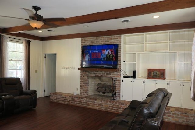 living room with ceiling fan, dark wood-type flooring, beamed ceiling, and a brick fireplace