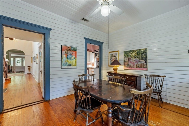 dining room featuring hardwood / wood-style floors, ceiling fan, and wooden walls