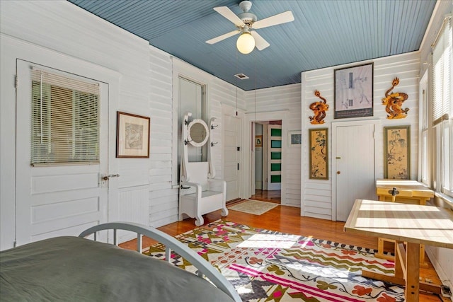 bedroom with hardwood / wood-style flooring, wood walls, and ceiling fan