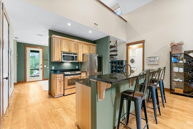 kitchen featuring stacked washer and clothes dryer, a breakfast bar area, stainless steel appliances, visible vents, and light wood-type flooring