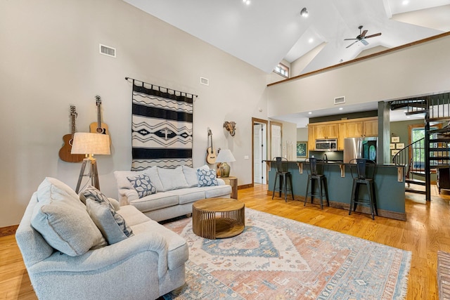 living room with a ceiling fan, visible vents, stairway, and light wood finished floors