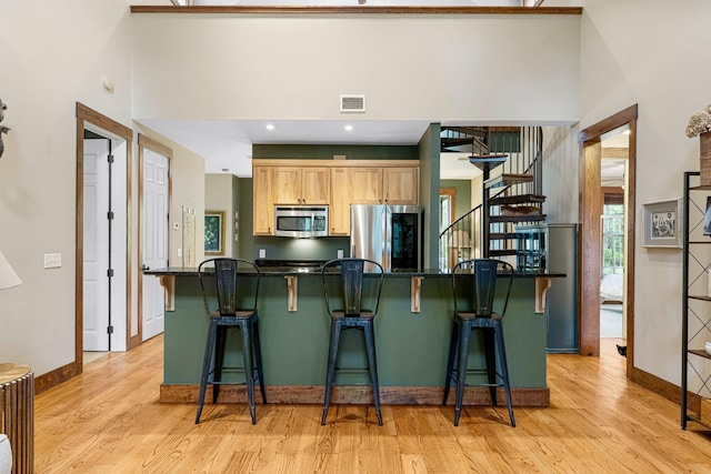 kitchen with stainless steel appliances, dark countertops, visible vents, light wood-style flooring, and light brown cabinetry