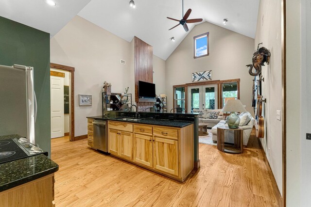 kitchen with open floor plan, stainless steel dishwasher, light wood-style floors, high vaulted ceiling, and a sink