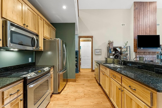 kitchen featuring a sink, visible vents, appliances with stainless steel finishes, light wood finished floors, and dark stone countertops