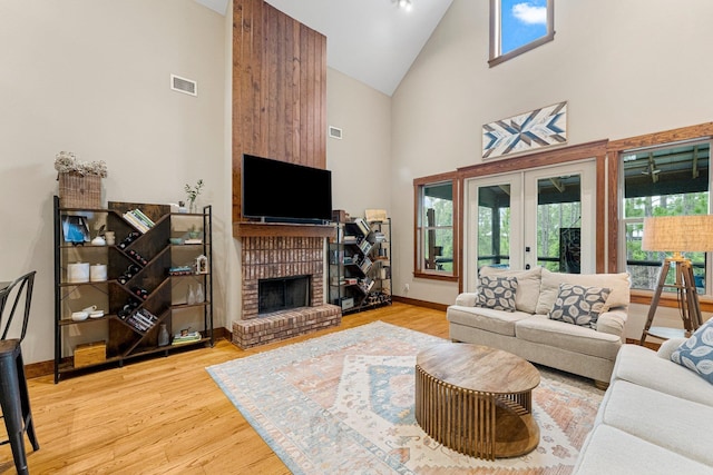 living area featuring baseboards, visible vents, light wood-style floors, a brick fireplace, and high vaulted ceiling