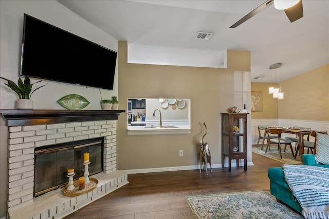 living room with ceiling fan with notable chandelier, sink, hardwood / wood-style flooring, and a fireplace