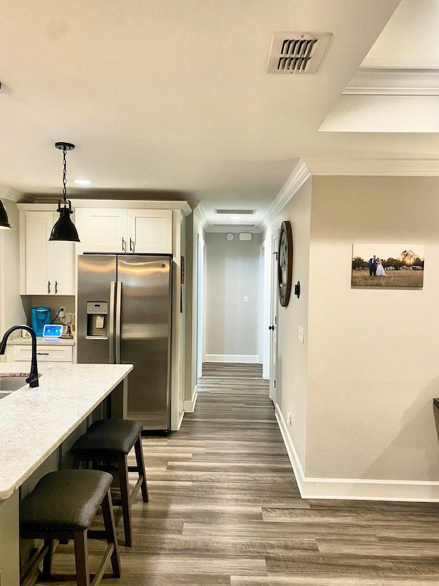 kitchen with stainless steel refrigerator with ice dispenser, white cabinetry, a kitchen breakfast bar, ornamental molding, and dark hardwood / wood-style flooring