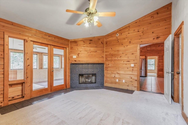 unfurnished living room with french doors, wood walls, vaulted ceiling, carpet flooring, and a tiled fireplace