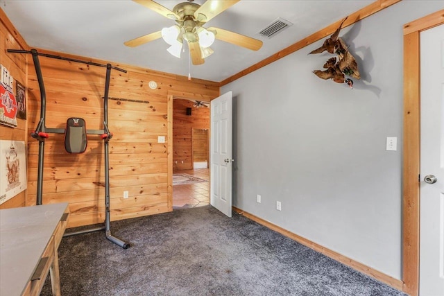 exercise room with dark colored carpet, ceiling fan, and wood walls