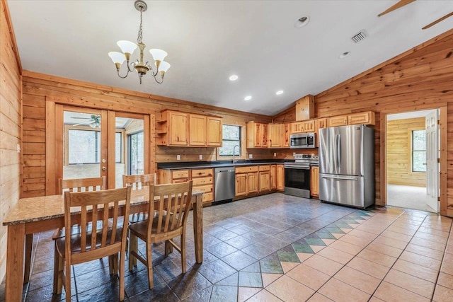 kitchen with vaulted ceiling, wood walls, decorative light fixtures, sink, and stainless steel appliances