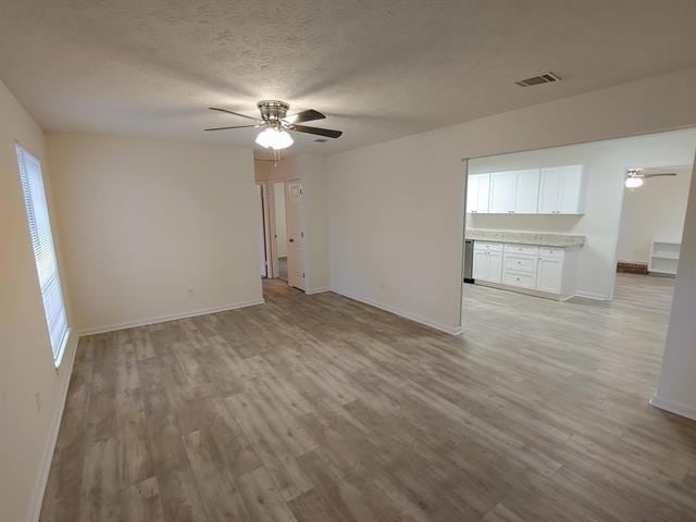 empty room featuring ceiling fan, plenty of natural light, a textured ceiling, and light wood-type flooring