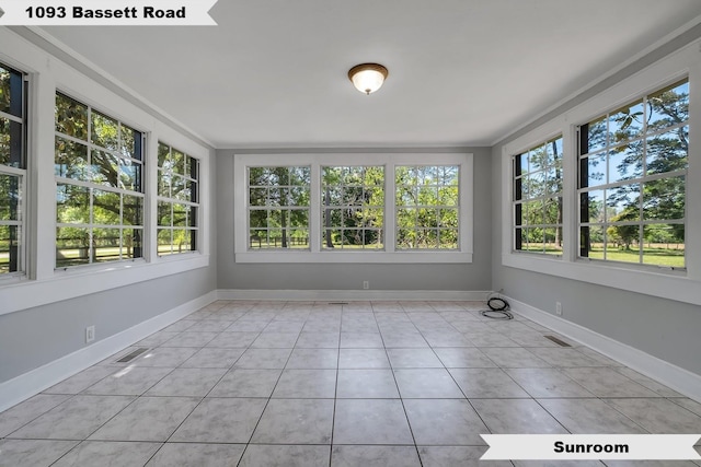 unfurnished sunroom with baseboards, tile patterned flooring, visible vents, and plenty of natural light
