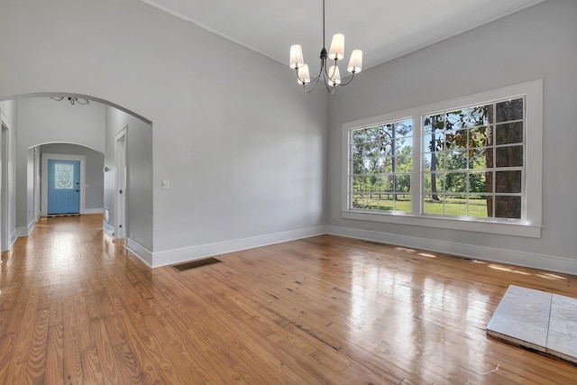 spare room featuring wood-type flooring, baseboards, arched walkways, and a chandelier